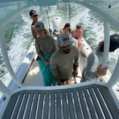 Six people enjoy an excursion on a motorboat, some standing and some sitting, as it speeds across the water and leaves a foamy wake behind.